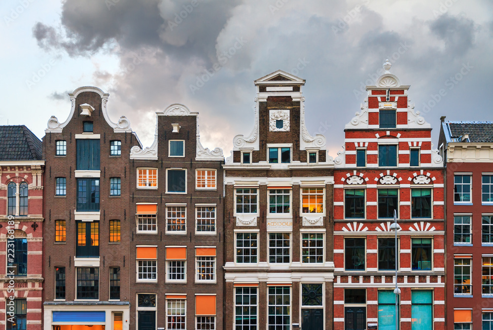 Fototapeta premium Fasady typowych holenderskich dworków nad kanałami światowego dziedzictwa UNESCO w Amsterdamie w Holandii, z letnim niebem o zachodzie słońca