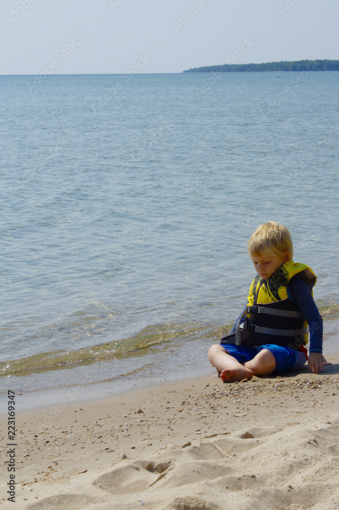 Cute Young Blonde School Aged Boy Sitting on Sunny Beach Looking Sadly Down at Sand Cute Young Blonde School Aged Boy Sitting on Sunny Beach Looking Sadly Down at Sand
