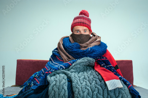 Bearded sick man with flue sitting on sofa at home or studio covered with knitted warm clothes. Illness, influenza, pain concept. Relaxation at Home. Healthcare Concepts. photo