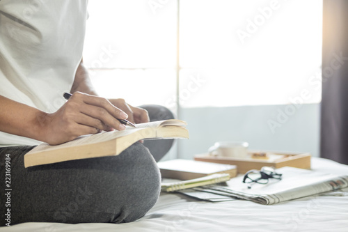 Young woman sitting working and writing in the notebook on bed leisure concept taking notes, Comfortable female workplace. Memories, planning , education.