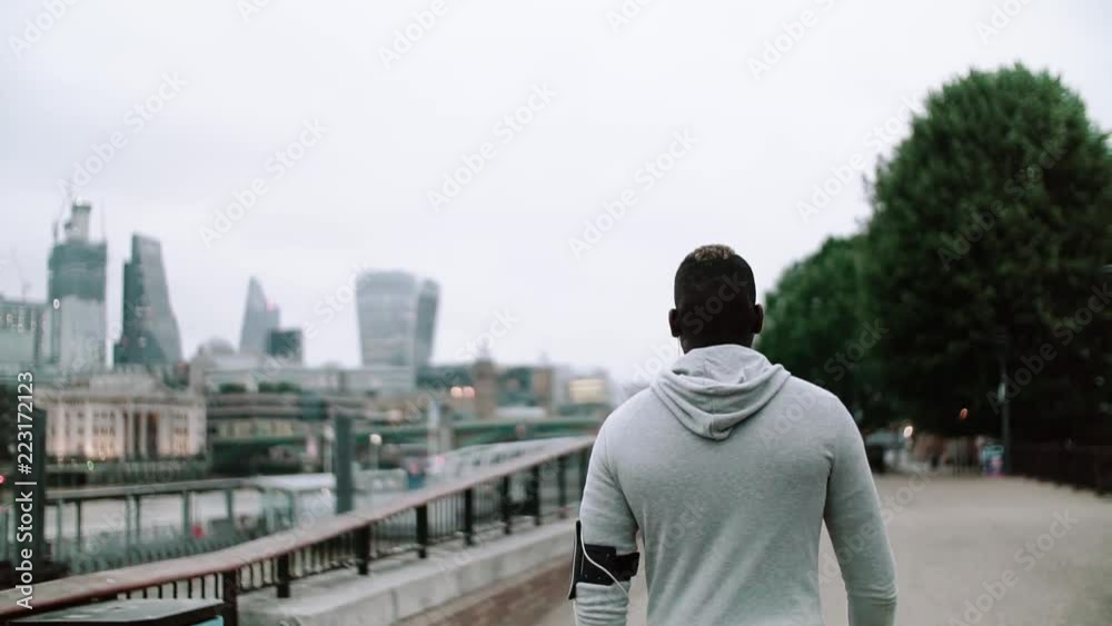 A rear view of young sporty black man runner with smart phone walking on the bridge in a city. A rear view of young sporty black man runner with smart phone walking on the bridge in a city.