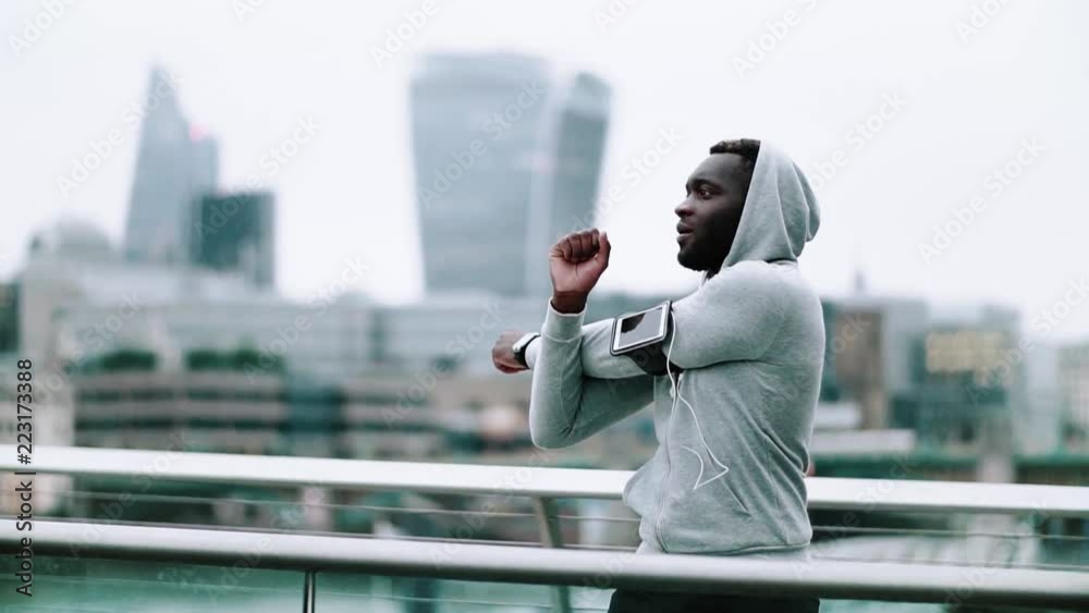Black man runner with smartphone in an armband on the bridge in a city, stretching. Black man runner with smartphone in an armband on the bridge in a city, stretching.