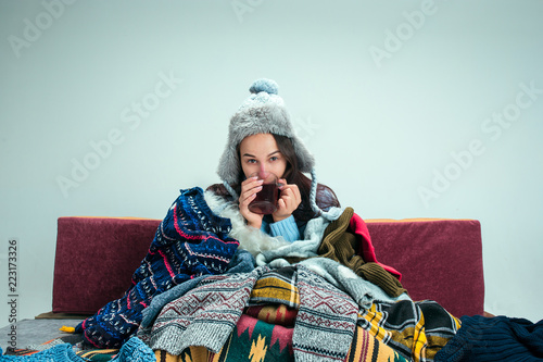 The young sick woman with flue sitting on sofa at home or studio covered with knitted warm clothes. Illness, influenza, pain concept. Relaxation at Home. Healthcare Concepts.
