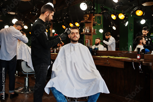 Handsome bearded man at the barbershop, barber at work, using hair dryer.