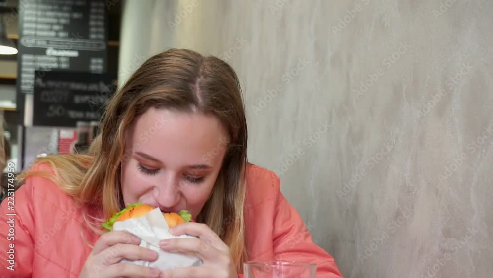 A young girl eating a hamburger. Sitting at a table in a cafe. Slow-mo A young girl eating a hamburger. Sitting at a table in a cafe. Slow-mo