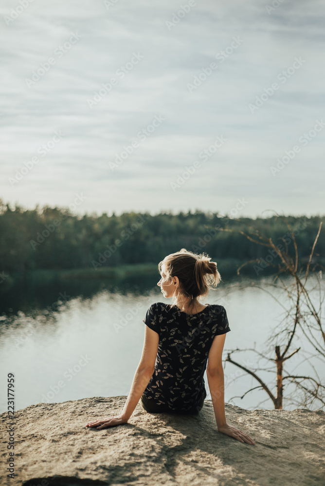 Young girl sitting on a hill overlooking the river and mountains. Lifestyle adventure vacations concept Young girl sitting on a hill overlooking the river and mountains. Lifestyle adventure vacations concept