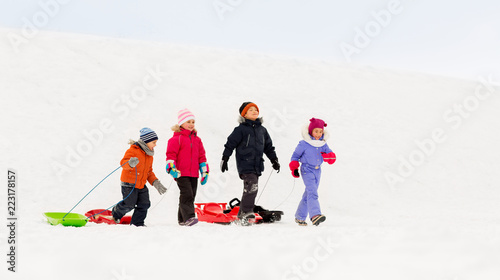 childhood, sledging and season concept - group of happy little kids with sleds in winter