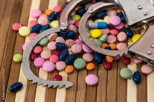 Tablets of different color on wooden table with handcuffs