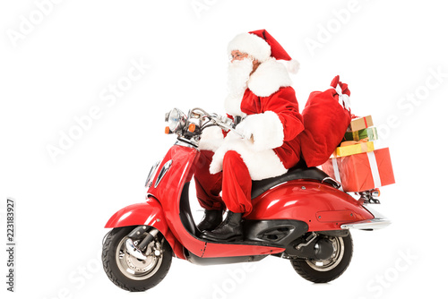 side view of santa claus riding vintage red scooter with sacks and gift boxes isolated on white