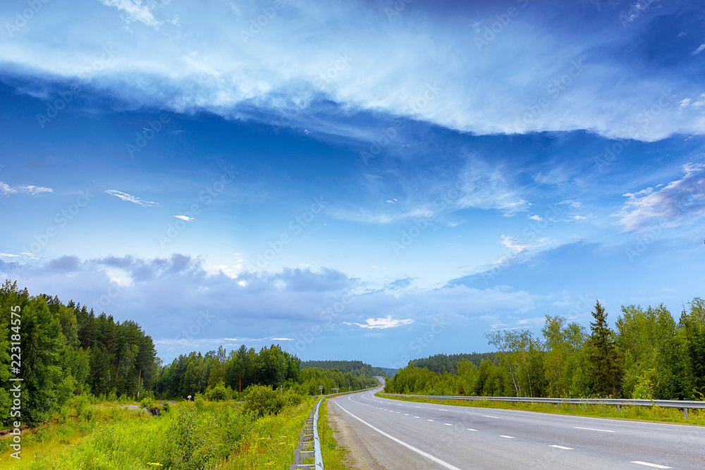 Fototapeta premium asphalt road through the forest with clouds, summer
