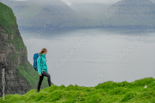 COPY SPACE: Young woman looks down at the ocean while hiking up a grassy hill.
