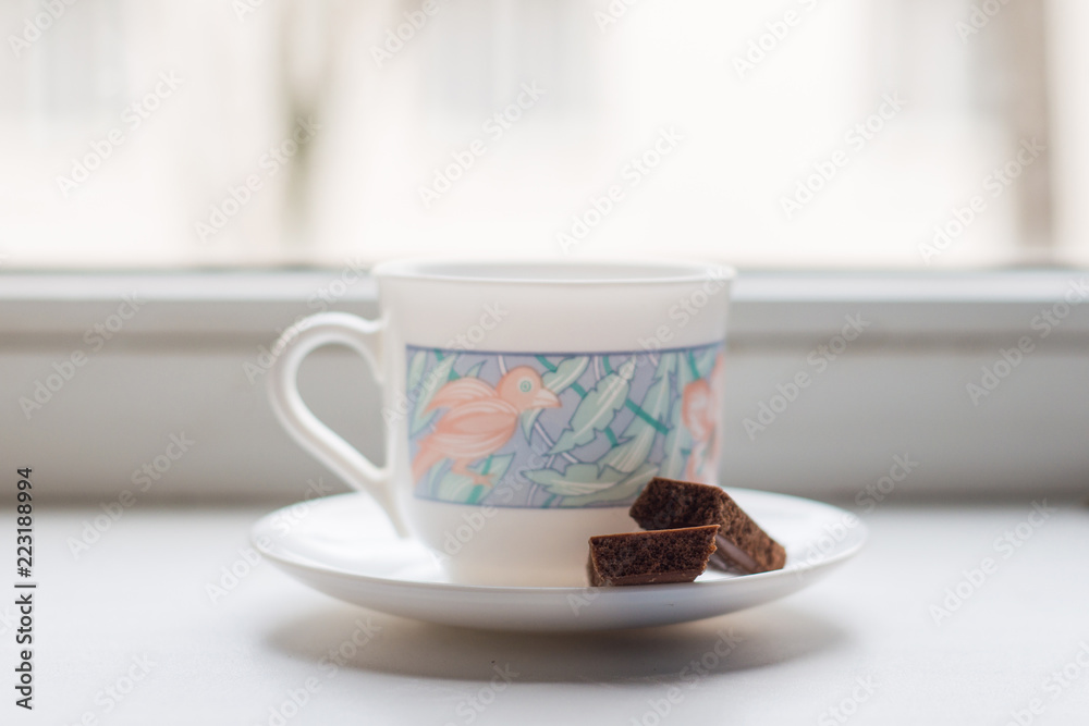 a Cup of fresh hot coffee and a pair of porous chocolate bars on a plate, on the background of the window