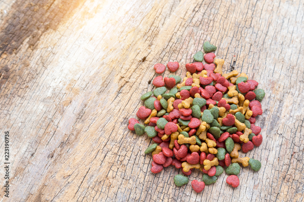 Pile of dry dog food on wooden background. Dog food 3 shapes 3 color. Mixing of Red heart, Light brown bone and Green vegetable. Pet food.