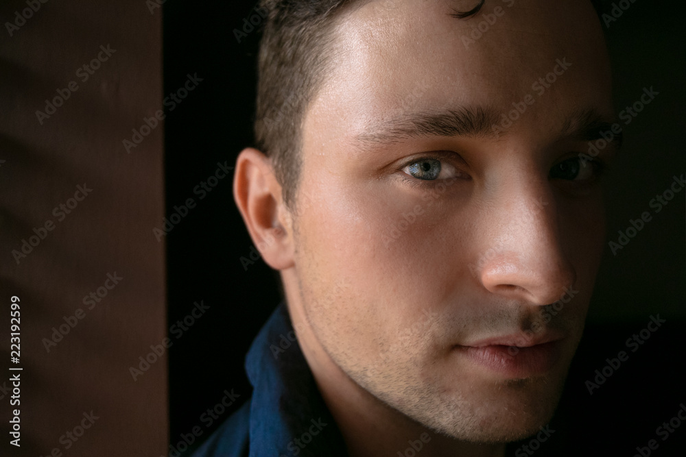 Fototapeta premium Good looking man with striking blue eyes stands in front of window