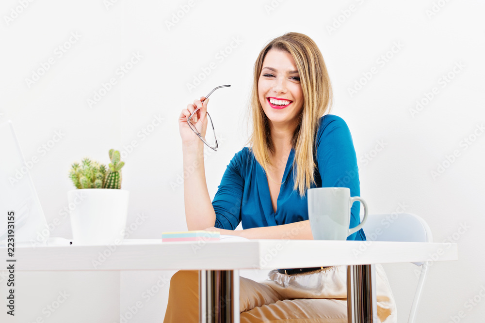 Young businesswoman smiling, sitting in her office holding eyeglasses, posing. Studio lighting, no retouch, bright vibrant colors. Young businesswoman smiling, sitting in her office holding eyeglasses, posing. Studio lighting, no retouch, bright vibrant colors.