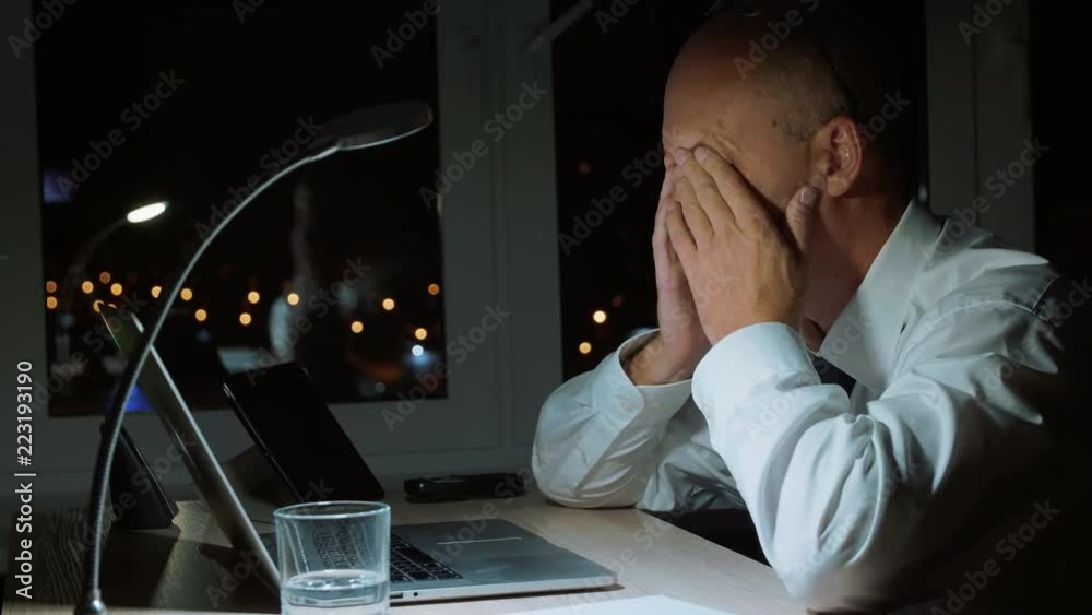 Executive businessman rubbing eyes while hard work by notebook in night office