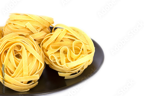 Uncooked tagliatelle on a black ceramic plate. Isolated