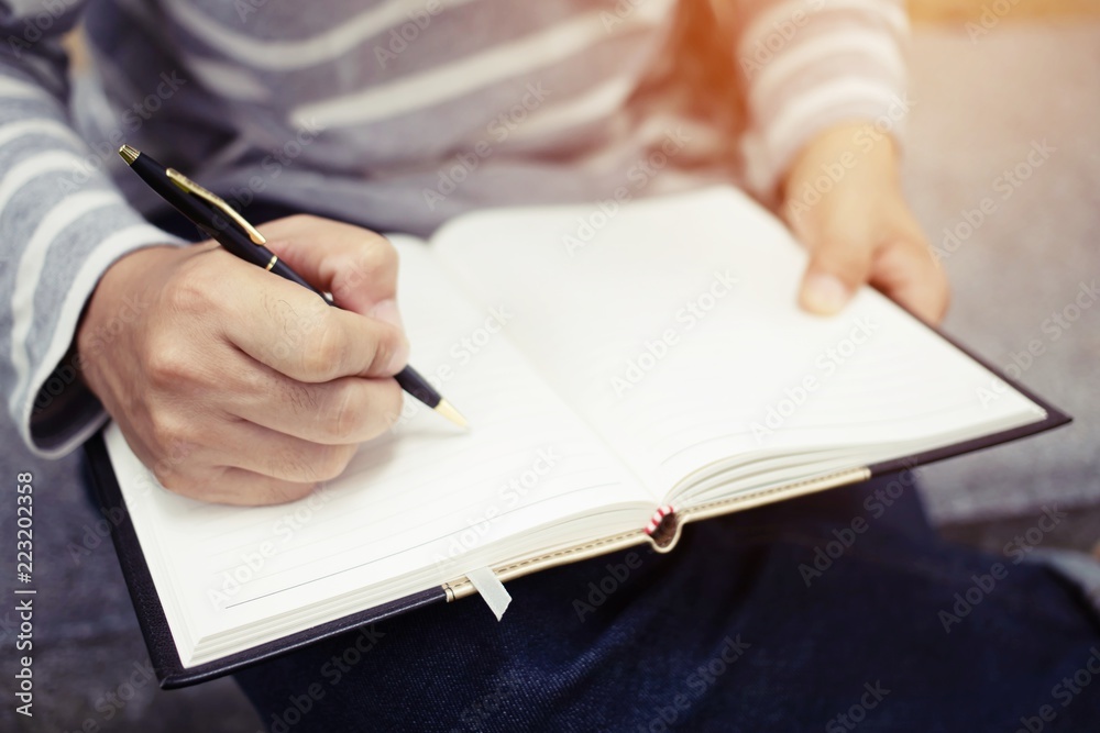 close up hand young man are sitting on a marble chair. using pen writing Record Lecture note pad into the book in park public. close up hand young man are sitting on a marble chair. using pen writing Record Lecture note pad into the book in park public.