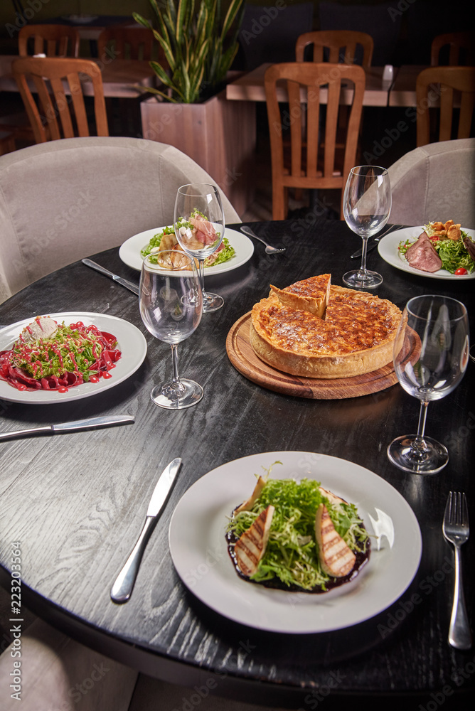 Chic black table with a variety of delicious dishes from the chef in a cafe, restaurant. The dining table is ready and reserved for guests. Cheese cake in the center of the table. Chic black table with a variety of delicious dishes from the chef in a cafe, restaurant. The dining table is ready and reserved for guests. Cheese cake in the center of the table.