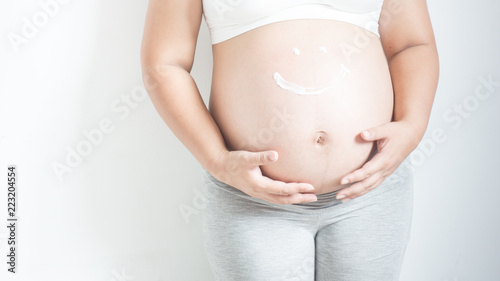 Pregnant Woman, Care. people and maternity concept - close up of pregnant woman applying with smile shape stretch mark cream to belly