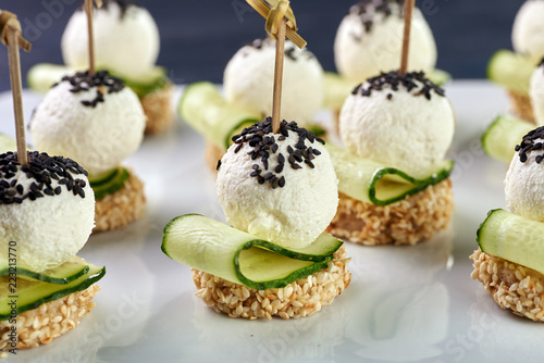 An unusual beautiful appetizing appetizer for a festive table. Mini canapes from a piece of baguette with sesame, thin slice of cucumber and a ball of cheese. Exotic black sesame for decoration.