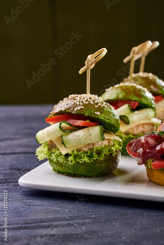 Fashionable set of multi-colored small hamburgers. Snack in the form of sandwiches with different fillings on a square plate. A treat for a buffet. Vegetarian and meat burgers.