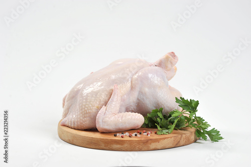 Chicken carcass raw on a round wooden board. On the board next to the chicken is the green of parsley and spices. White background. Close-up. 