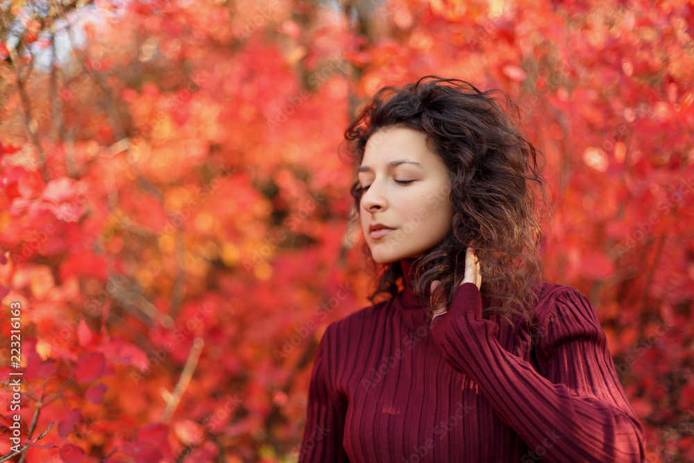 Young blackhaired woman in red sweather posing on camera in red autumnn bushes Young blackhaired woman in red sweather posing on camera in red autumnn bushes