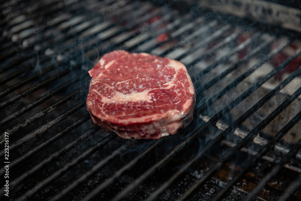 A perfect 1 inch thick New York strip loin steak, seasoned and grilling over the flame on the barbecue