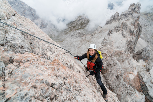 young attractive female university student on a steep and exposed rock face climbs a Via Ferrata in Alta Badia in the South Tyrol