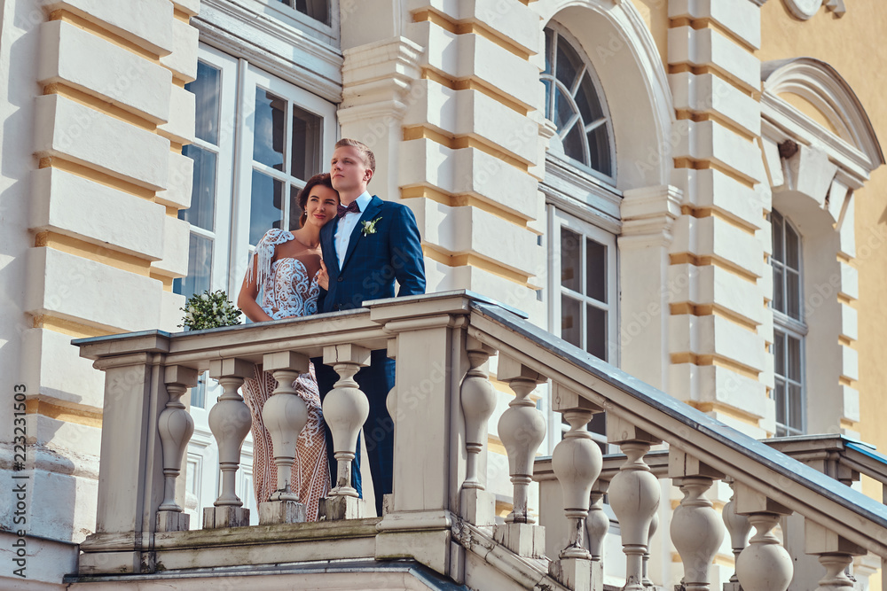 Full body portrait of happy newlyweds embracing while posing on the stairs of the beautiful old palace. Full body portrait of happy newlyweds embracing while posing on the stairs of the beautiful old palace.