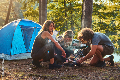 Three friends hiking in the forest and try to light a fire at camp.