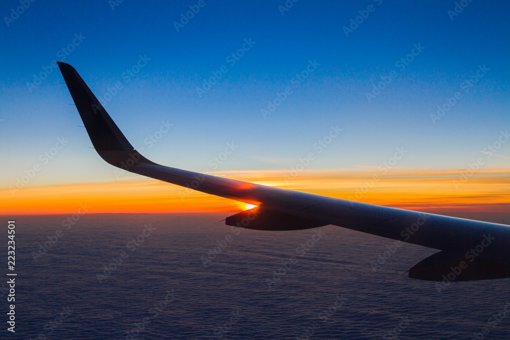 Obraz premium Blue planet Earth sky seen through an airplane window. Unique panoramic high altitude aerial view of a flaring tropical sunset in the cloudscape horizon behind the aircraft wing.
