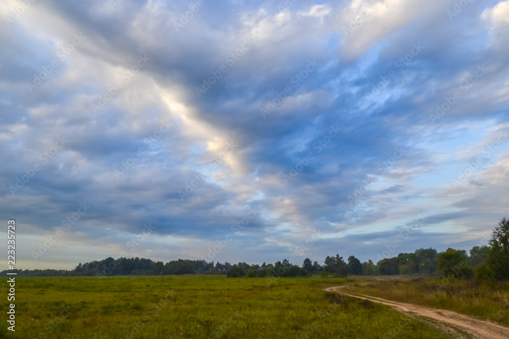 Road through fields and clouds to the sky