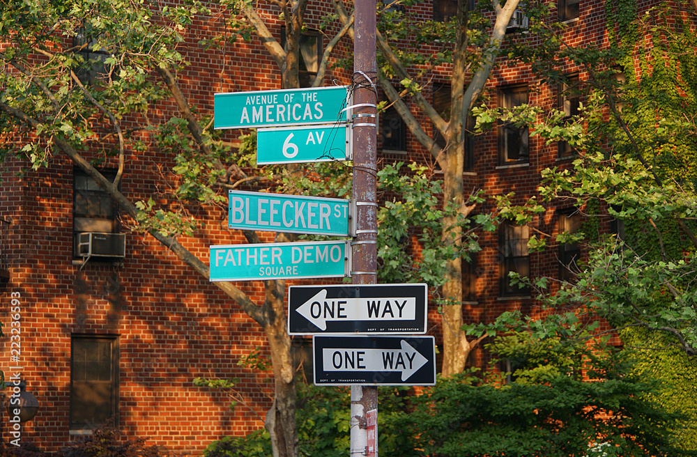 Street sign for Avenue of the Americas, 6th Ave, Blecker Street, Father Demo Square, one way arrow direction with buildings and trees in background on Manhattan, New York City, United States. (2009)