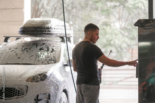 Fotografija A man washes his car in a self-service sink and pays for the supply of liquid in the bill acceptor machine