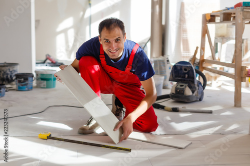 Fotografija Master is wearing work clothes, is checking horizon of installing tiles, using b