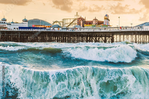 Brighton Pier, Brighton, Sussex, Britain on a storm evening at dusk as the sun is setting. There are high waves and surf on the beach photo