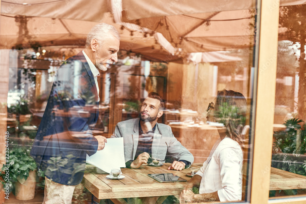 Business lunch. Three people in the restaurant sitting at table discussing project outside the window view. Team work concept