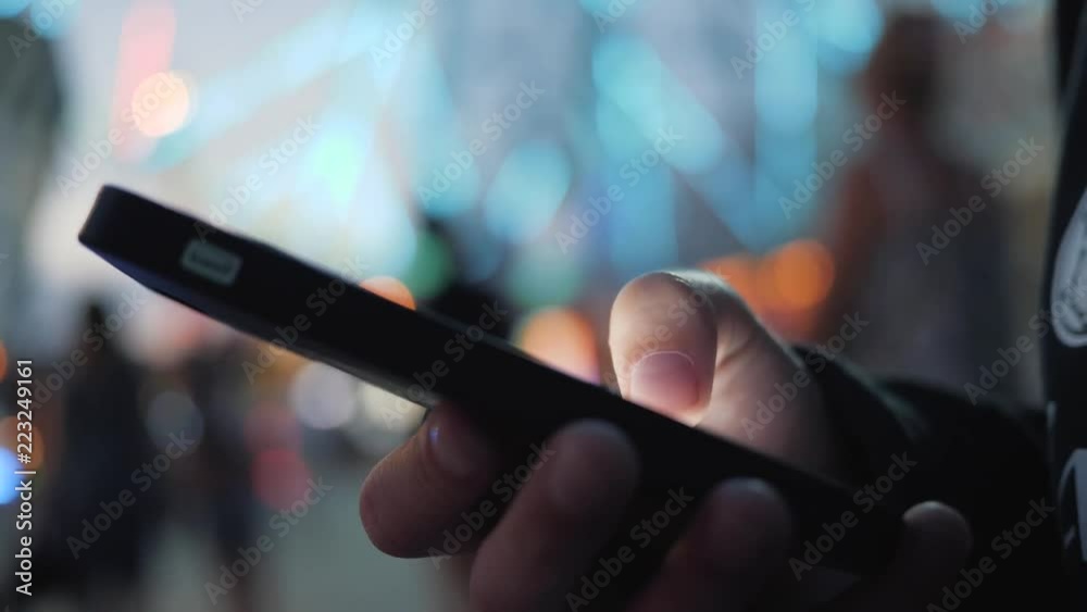 Close-up image of a child's hands using a smartphone at night on a city shopping street, search or social network concept, a hipster man typing a sms message to his friends