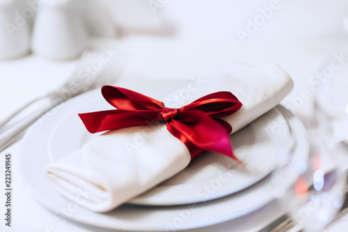 Close-up of a white napkin with a beautiful red bow on the plate
