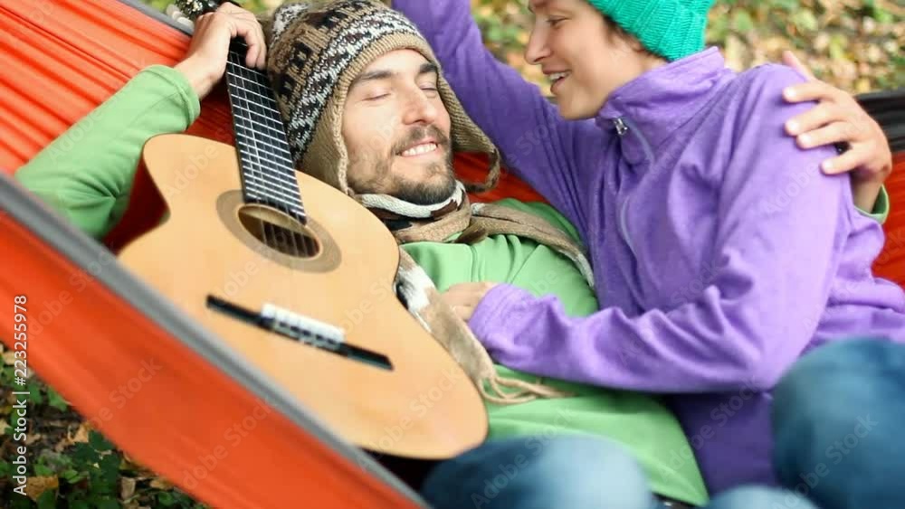 Happy couple chilling in hammock in autumn forest. They kiss, smile and talk. Guitar lying nearby. Happy couple chilling in hammock in autumn forest. They kiss, smile and talk. Guitar lying nearby.
