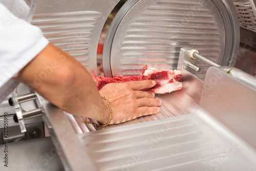 hand of butcher using slicer in butcher shop photo