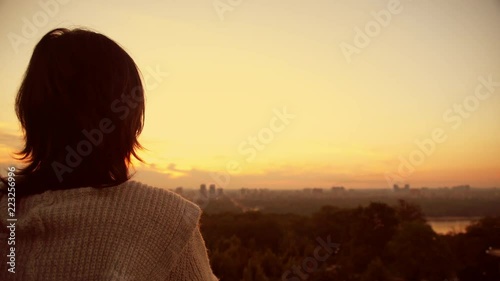 Red lights caused by the rays of the dawn romanticize the observing person. A woman perceives how delightful may nature be. Her dark hair seems red now.