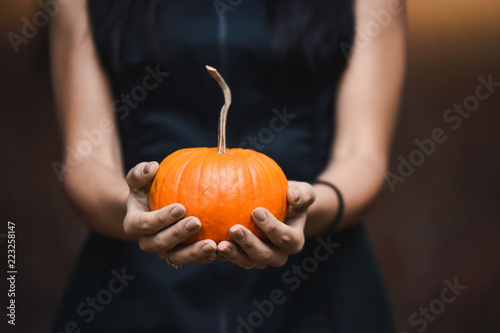 close-up of a young girl witch in black hat with orange pumpkin in hands holding a yellow autumn garden park celebrates Halloween with witchcraft