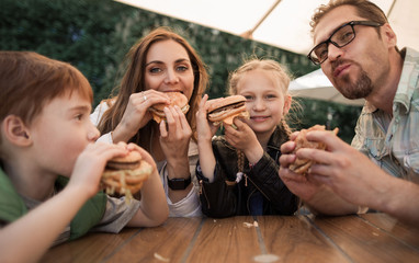 happy family eating burgers sitting at a table in a cafe