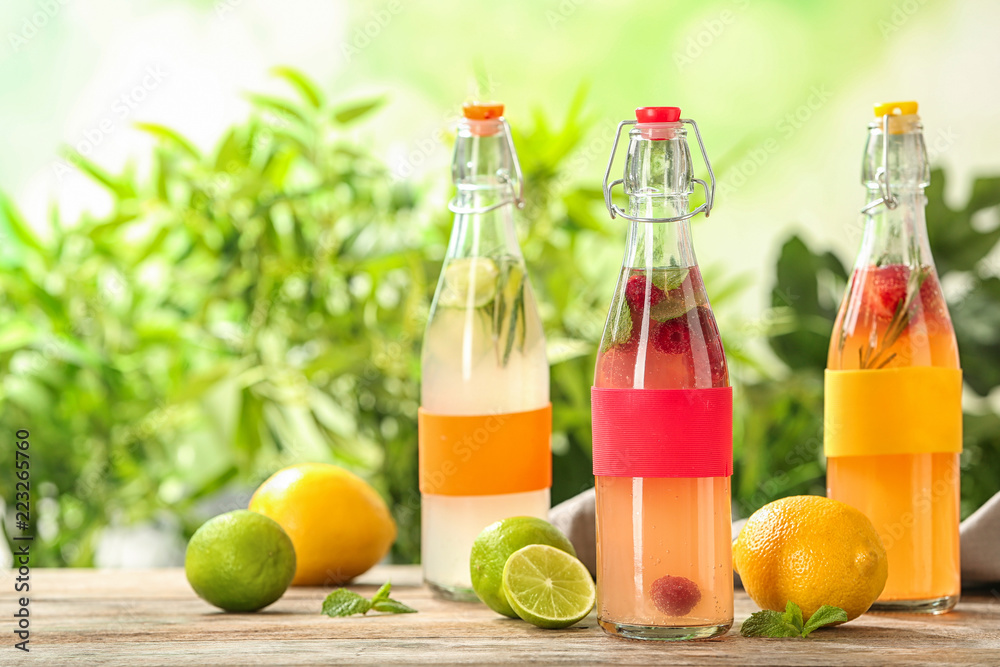 Bottles with natural lemonade on table against blurred background Bottles with natural lemonade on table against blurred background