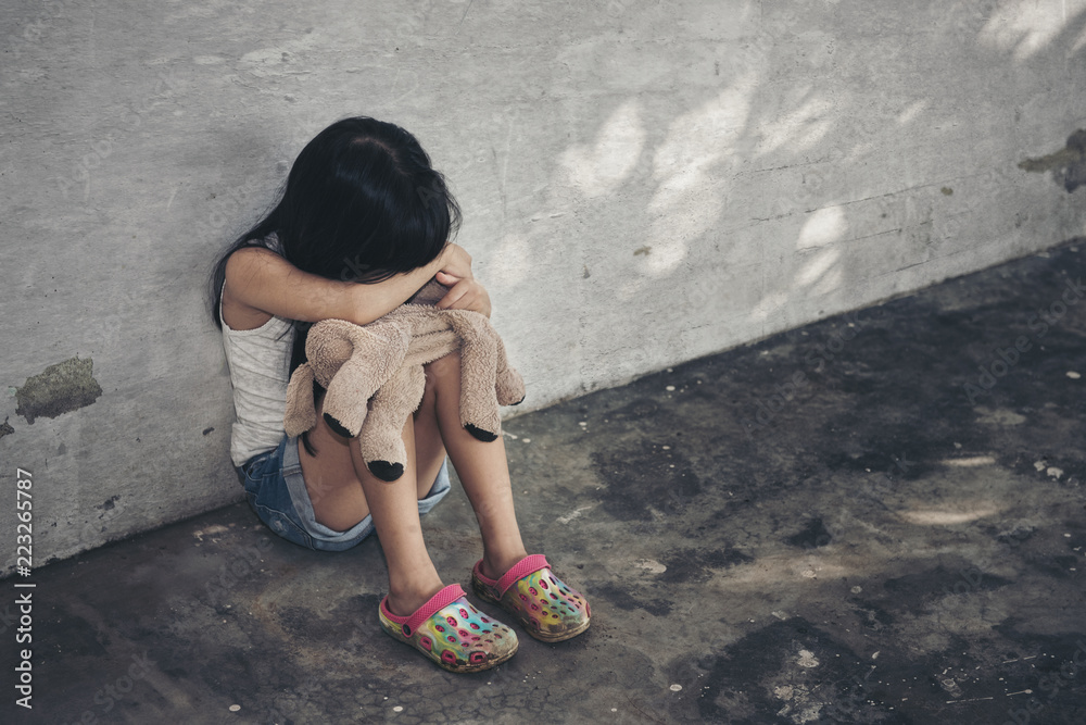 Little girl crying in the corner with doll. Domestic violence concept
