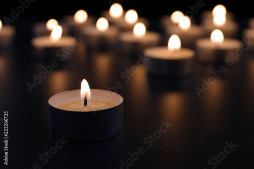 Burning candle on table in darkness  closeup with space for text. Funeral symbol