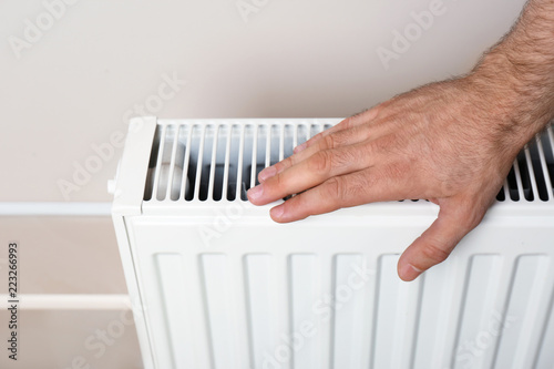 Man warming hand on heating radiator near color wall
